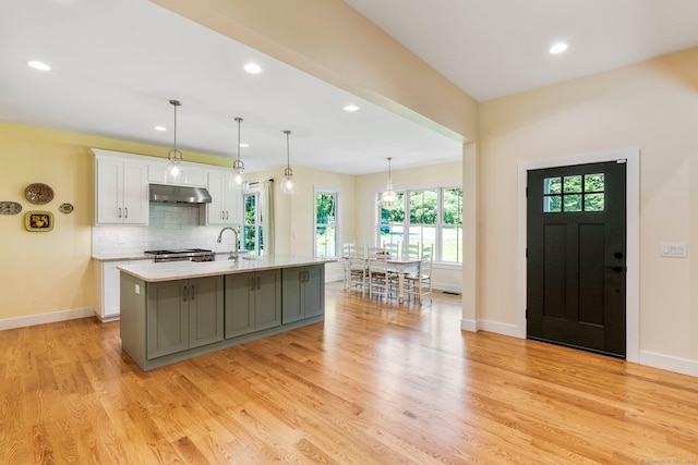 kitchen featuring white cabinets, an island with sink, a healthy amount of sunlight, and light wood-type flooring