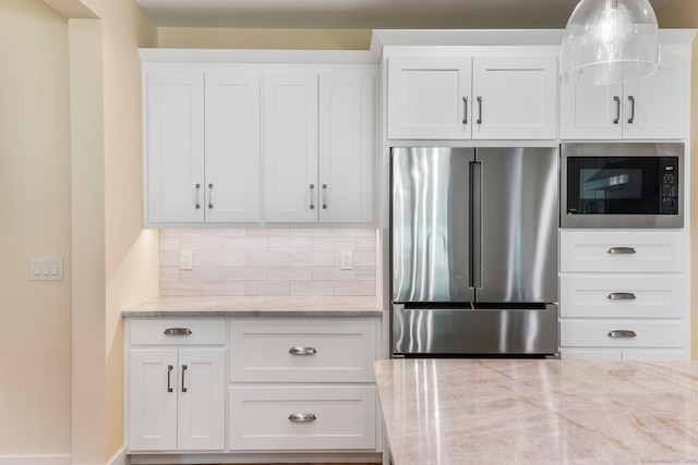 kitchen featuring high end refrigerator, built in microwave, tasteful backsplash, light stone counters, and white cabinetry