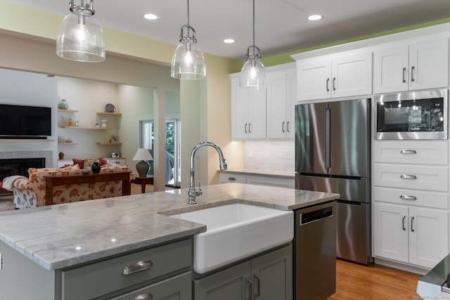 kitchen with sink, hanging light fixtures, a fireplace, white cabinetry, and stainless steel appliances