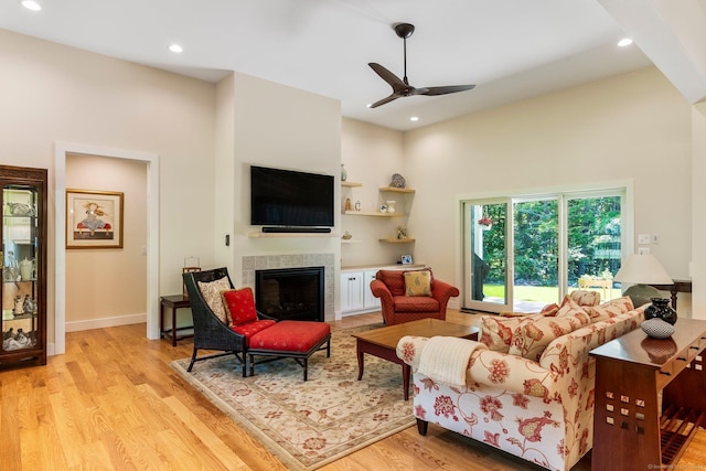 living room with a tiled fireplace, ceiling fan, and light wood-type flooring