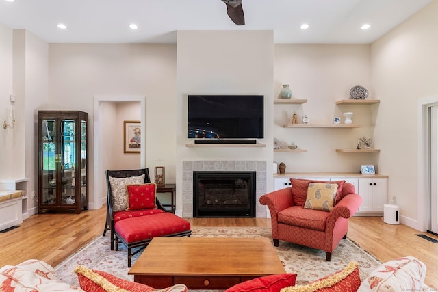 living room featuring a tile fireplace, ceiling fan, and light wood-type flooring