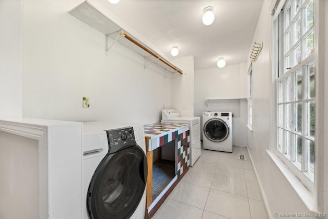 laundry room featuring light tile patterned flooring, a healthy amount of sunlight, and washer and dryer