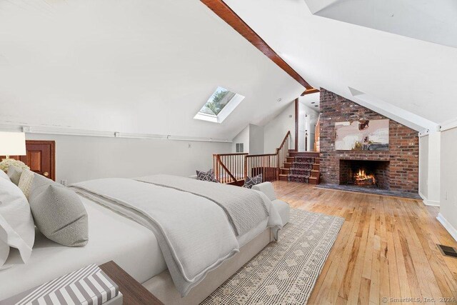 bedroom featuring vaulted ceiling with skylight, a fireplace, and light hardwood / wood-style flooring