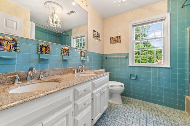 bathroom with tile walls, tile patterned flooring, an inviting chandelier, vanity, and toilet