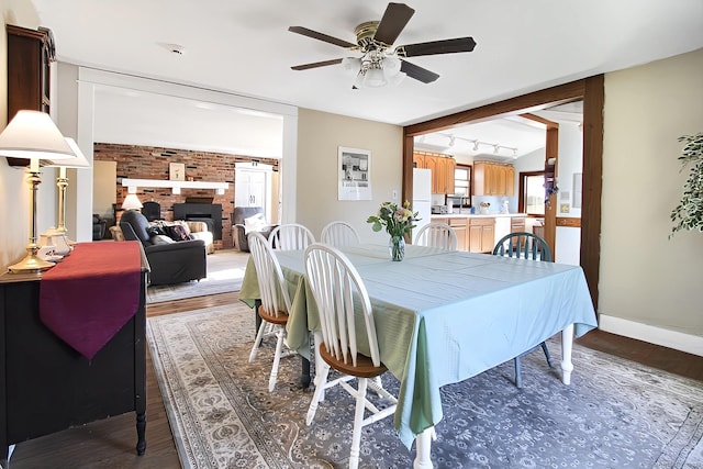 dining room featuring track lighting, a brick fireplace, ceiling fan, dark hardwood / wood-style flooring, and brick wall