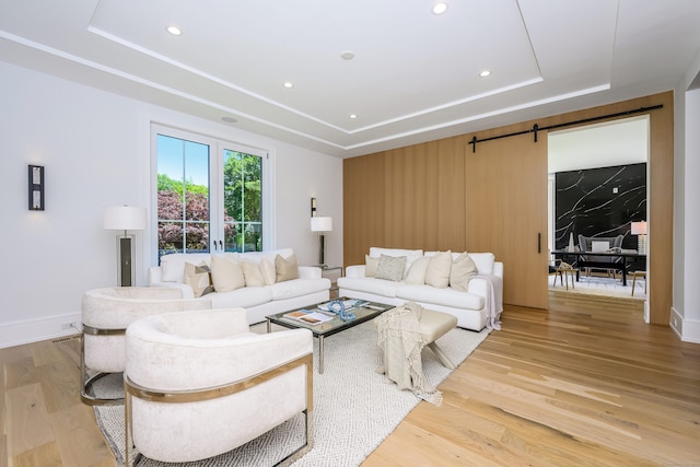 living room featuring a raised ceiling, a barn door, and light hardwood / wood-style flooring