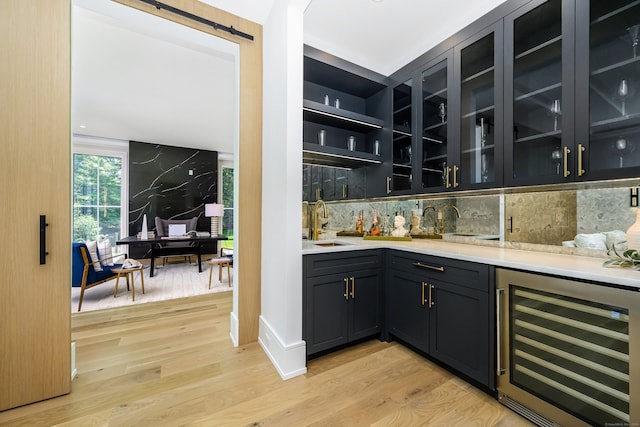 bar featuring tasteful backsplash, light hardwood / wood-style flooring, beverage cooler, and sink