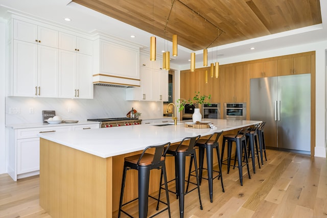 kitchen featuring appliances with stainless steel finishes, wood ceiling, a large island with sink, white cabinets, and hanging light fixtures