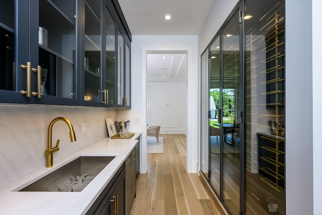 bar featuring light wood-type flooring, tasteful backsplash, stainless steel dishwasher, and sink