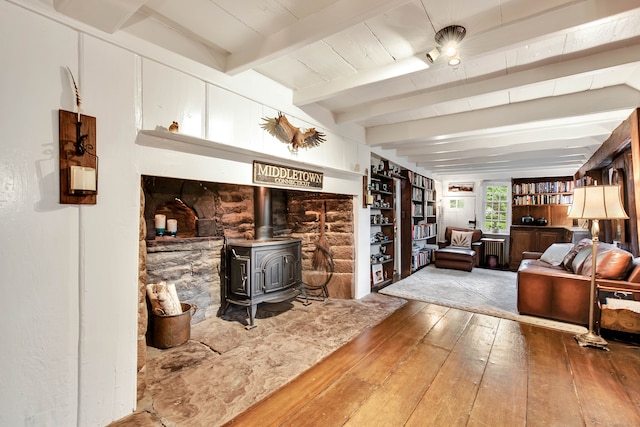 living room with beam ceiling, hardwood / wood-style flooring, and a wood stove