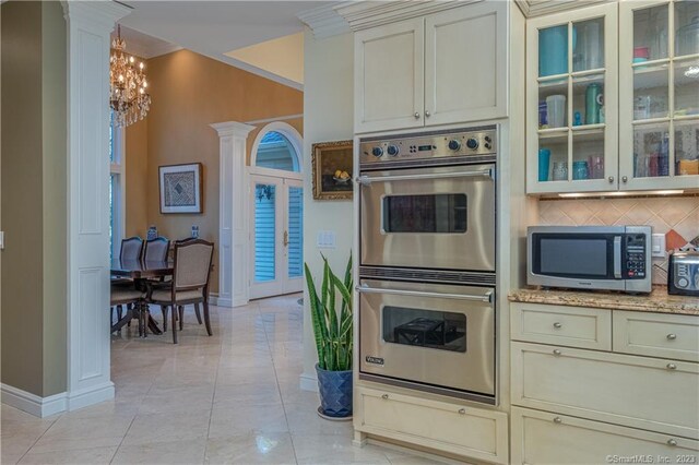 kitchen with a notable chandelier, tasteful backsplash, ornate columns, light tile floors, and appliances with stainless steel finishes