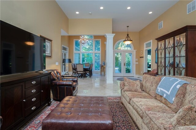 tiled living room featuring french doors, ornate columns, and an inviting chandelier