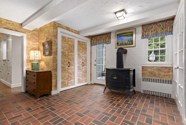 living room featuring a wood stove, radiator heating unit, and beam ceiling