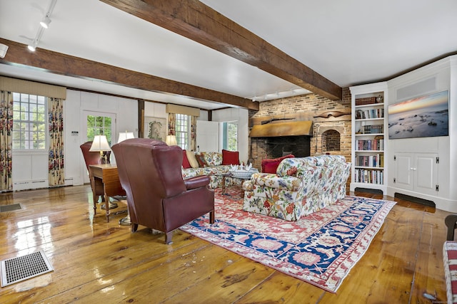 living room featuring a healthy amount of sunlight, beam ceiling, hardwood / wood-style floors, and a brick fireplace