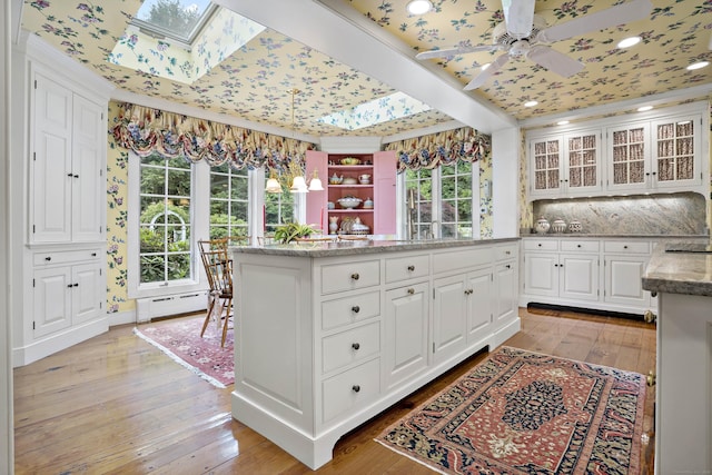 kitchen with light hardwood / wood-style flooring, baseboard heating, white cabinetry, light stone counters, and decorative light fixtures