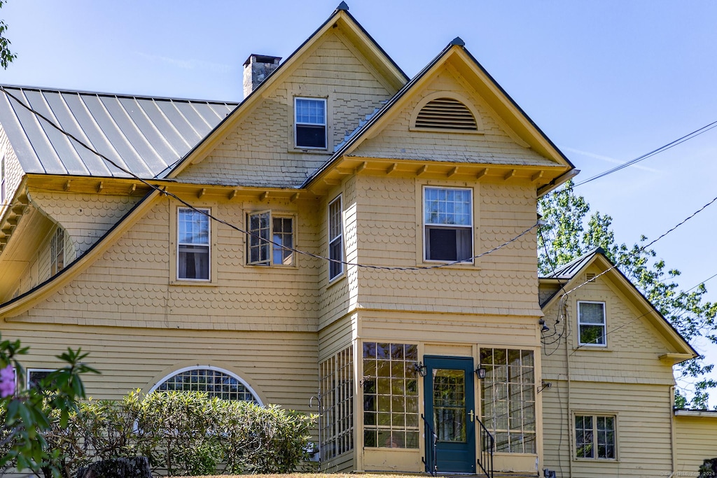 back of house with a standing seam roof, a chimney, and metal roof