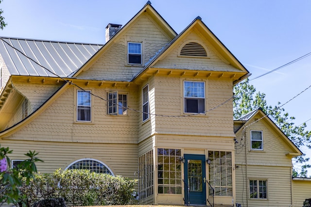 back of house with a standing seam roof, a chimney, and metal roof