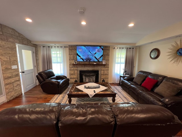 living room featuring hardwood / wood-style floors, vaulted ceiling, and a stone fireplace