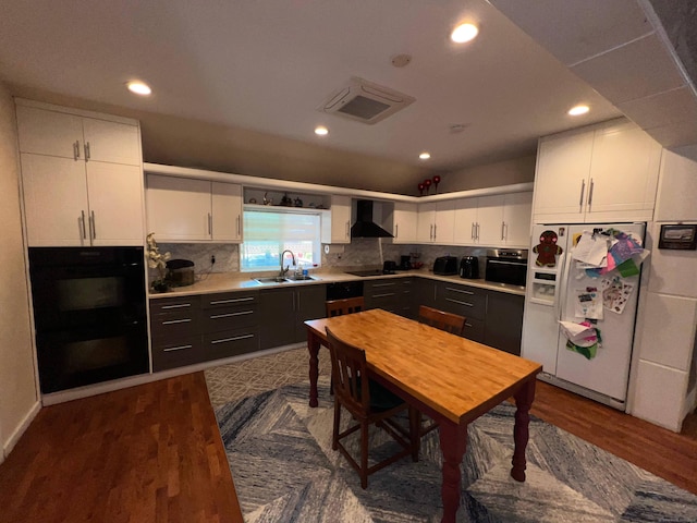 kitchen featuring wall chimney range hood, sink, wood-type flooring, black appliances, and white cabinetry