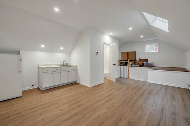 additional living space with vaulted ceiling with skylight and light wood-type flooring