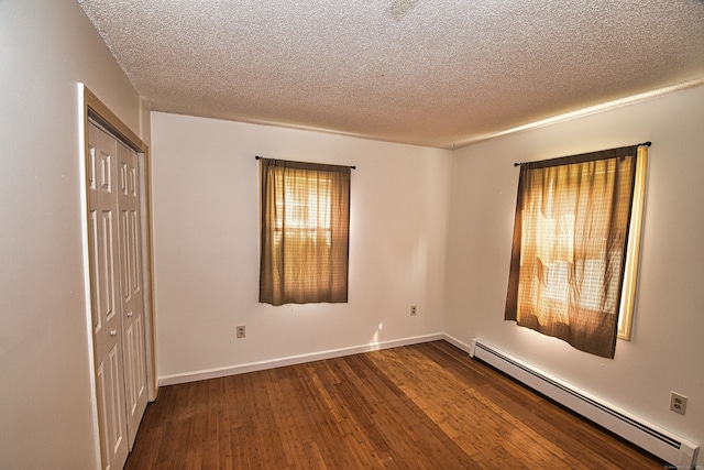 empty room featuring a textured ceiling, dark hardwood / wood-style flooring, and a baseboard heating unit