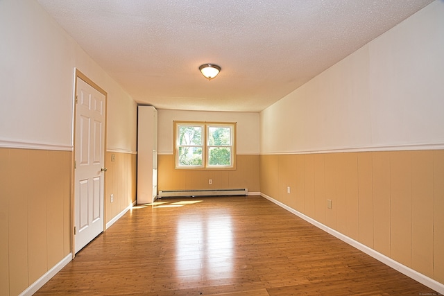 unfurnished room with wooden walls, a baseboard radiator, a textured ceiling, and wood-type flooring