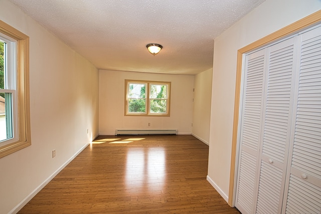 unfurnished bedroom with baseboard heating, multiple windows, a closet, and hardwood / wood-style floors