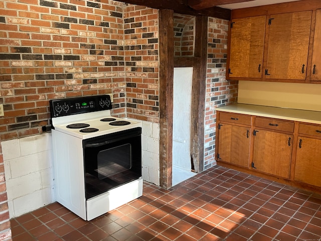 kitchen with dark tile patterned flooring, brick wall, and electric range