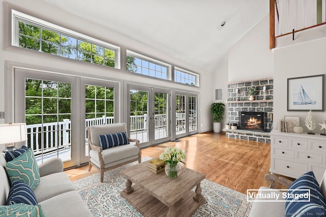 living room with a stone fireplace, light hardwood / wood-style flooring, high vaulted ceiling, and french doors