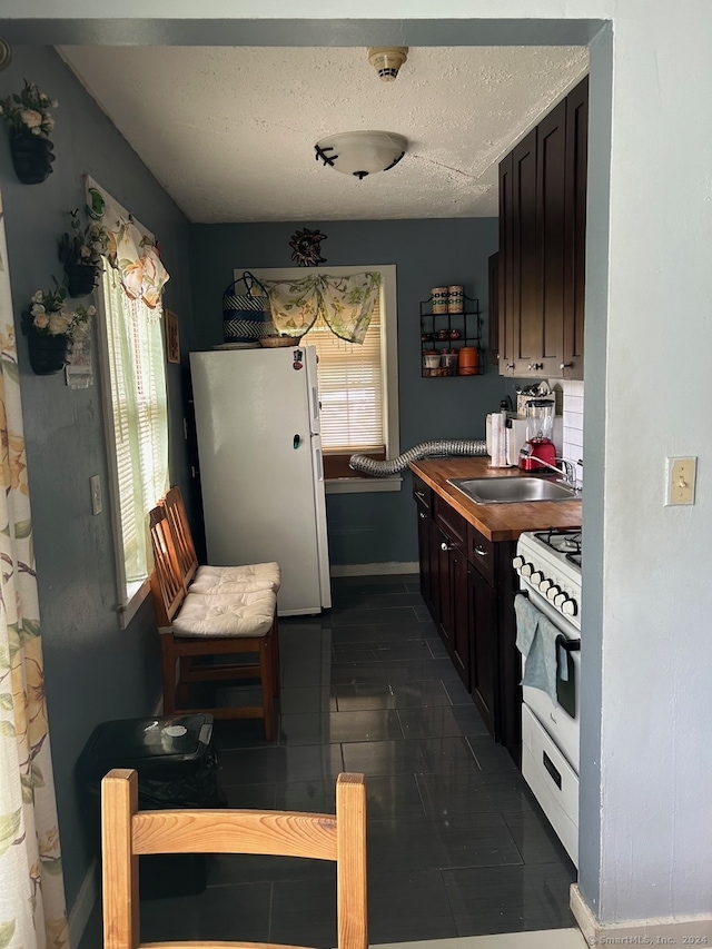 kitchen featuring white appliances, sink, dark tile flooring, and a textured ceiling