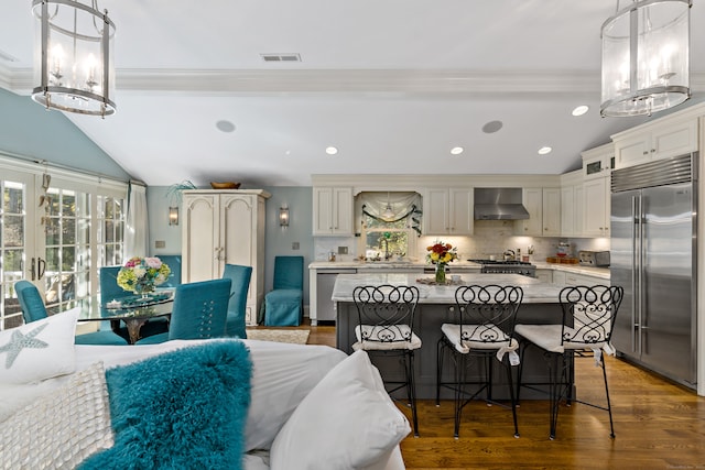 kitchen with a center island, stainless steel appliances, wall chimney exhaust hood, decorative light fixtures, and dark wood-type flooring