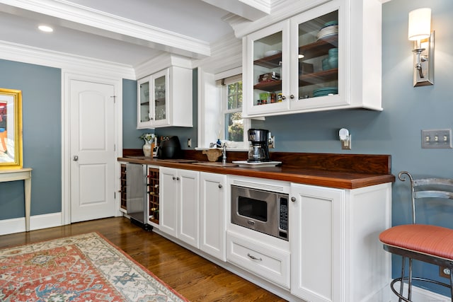 bar featuring beverage cooler, stainless steel microwave, dark hardwood / wood-style flooring, wooden counters, and ornamental molding