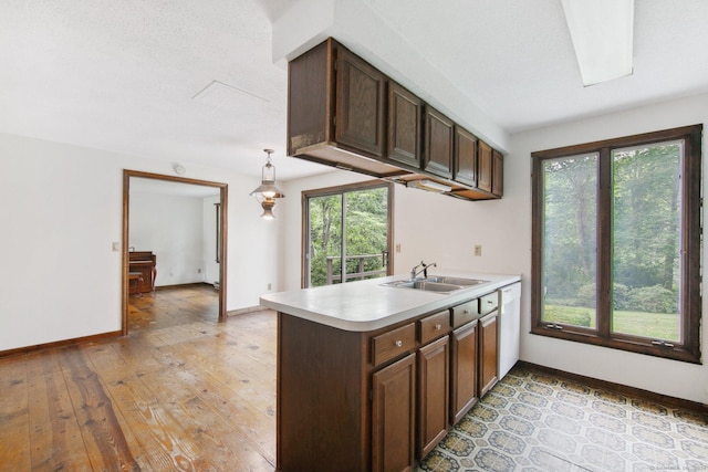 kitchen featuring kitchen peninsula, sink, hanging light fixtures, white dishwasher, and dark brown cabinetry