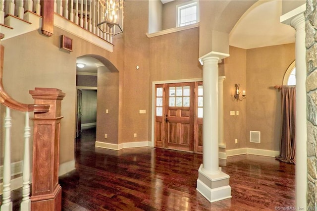 foyer featuring decorative columns, plenty of natural light, a towering ceiling, and dark wood-type flooring