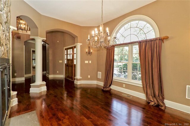 unfurnished dining area with a notable chandelier, vaulted ceiling, ornate columns, and dark hardwood / wood-style floors