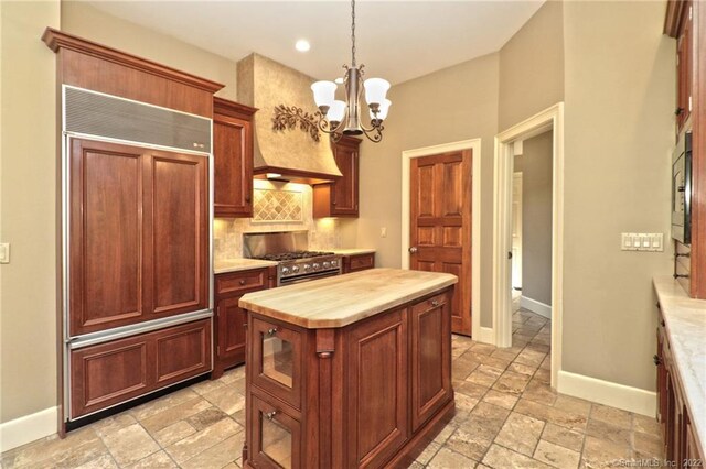 kitchen featuring built in appliances, tasteful backsplash, light tile patterned floors, butcher block counters, and a kitchen island