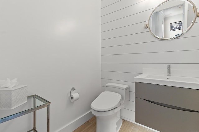 half bath with baseboards, wood finished floors, toilet, and vanity