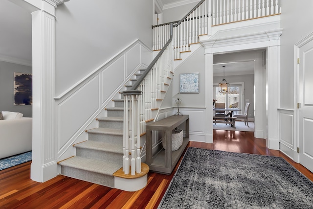 staircase with decorative columns, crown molding, a decorative wall, wainscoting, and wood finished floors