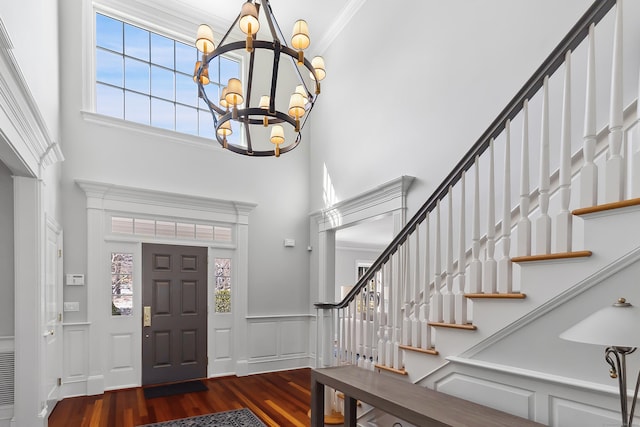 foyer entrance with a chandelier, wainscoting, wood finished floors, and a towering ceiling