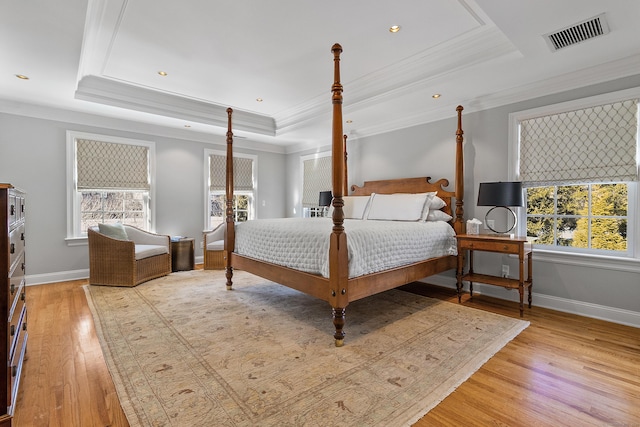 bedroom with a raised ceiling, visible vents, light wood finished floors, and multiple windows