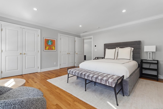 bedroom with crown molding, recessed lighting, two closets, and light wood-style floors