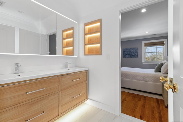 ensuite bathroom with connected bathroom, a sink, baseboards, visible vents, and crown molding