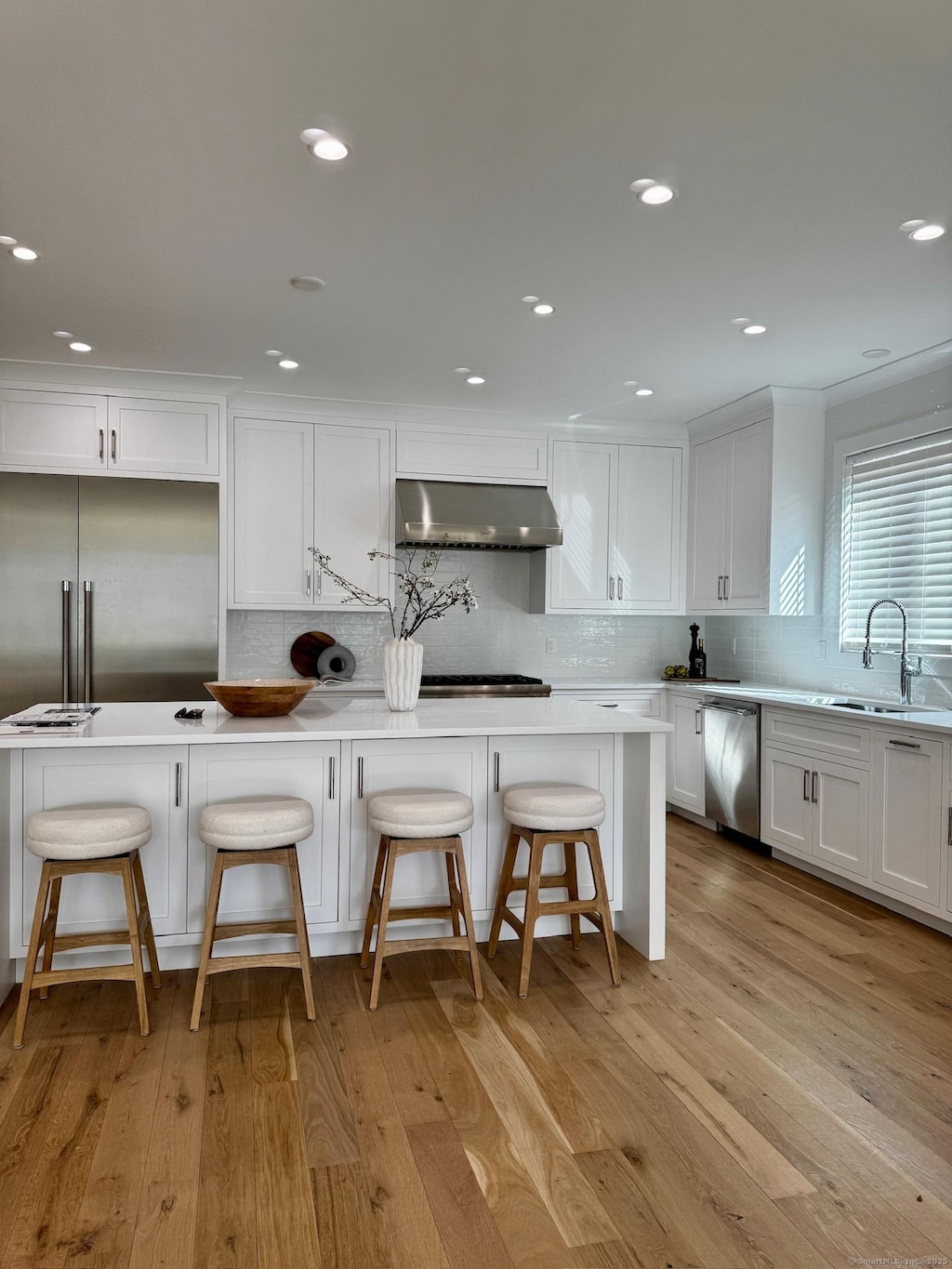 kitchen with a breakfast bar, light countertops, a sink, and under cabinet range hood