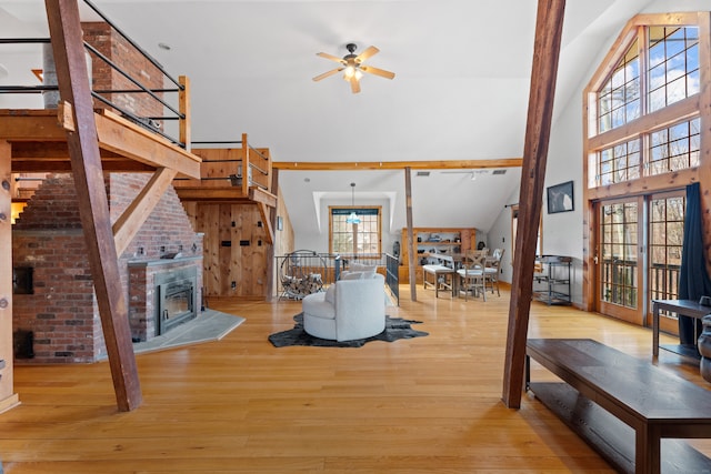 living room featuring high vaulted ceiling, ceiling fan, light wood-type flooring, and a fireplace