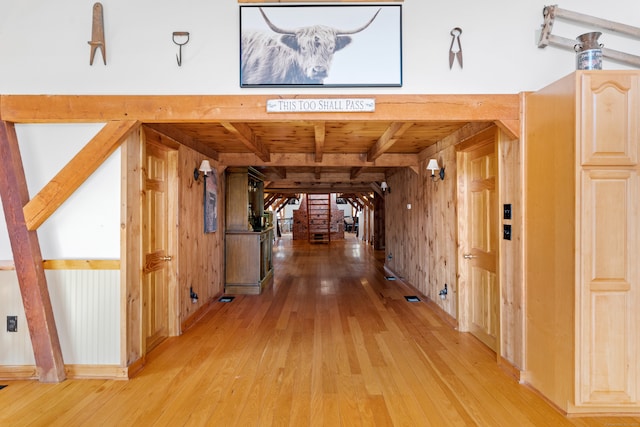 hall featuring beamed ceiling, wooden walls, and light wood-type flooring