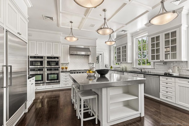 kitchen featuring wall chimney exhaust hood, hanging light fixtures, coffered ceiling, white cabinets, and appliances with stainless steel finishes