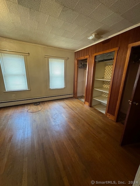 unfurnished bedroom featuring hardwood / wood-style floors, a baseboard radiator, wood walls, and multiple windows