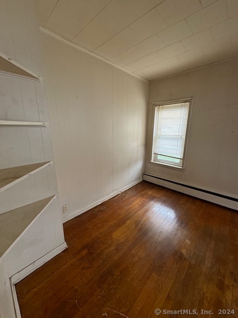 spare room featuring a baseboard heating unit and wood-type flooring