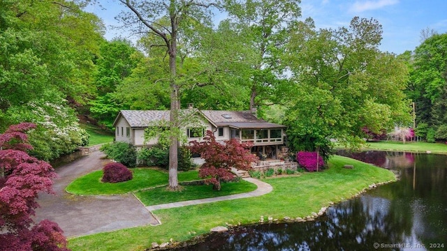 view of front facade with a front yard, a sunroom, and a water view