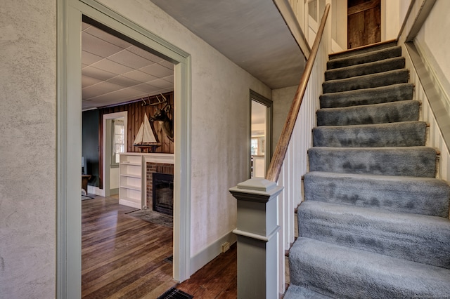 stairway featuring hardwood / wood-style floors, plenty of natural light, wood walls, and a brick fireplace